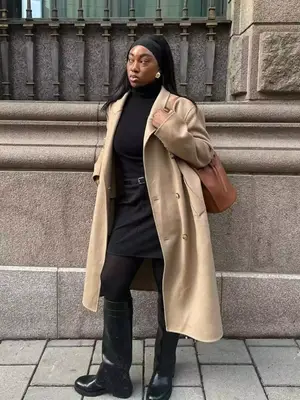 Nnenna Echem wears a long trench coat, black turtleneck, mini skirt, tights, tall boots, and cloth headband