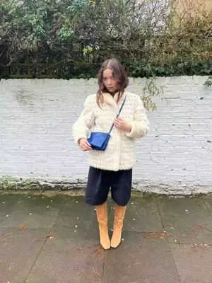 Junia wearing a white jacket, shorts, camel boots, and a bright blue crossbody bag