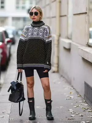 Model wearing a printed sweater, bike shorts, and hunter boots. She