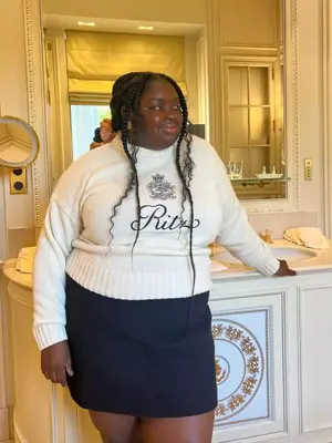 Abisola Omole wearing a white sweater and black mini skirt with a pink accessory in her hair