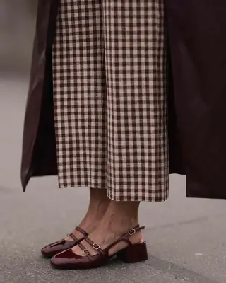 Close-up of person wearing Mary Jane heels, gingham pants, and longline coat