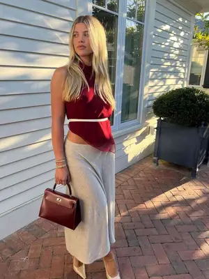 Sofia Richie Grainge wears a red top, thin white belt, gray skirt and cream heels. 