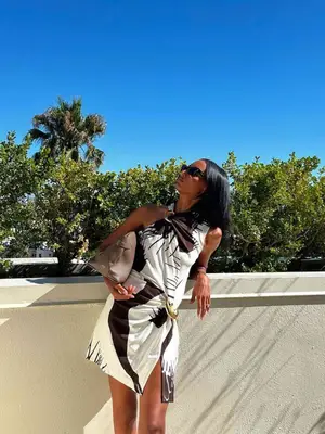 Jasmine Tookes wears an abstract-print mini dress, sunglasses, and a brown bag
