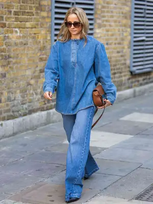 Woman wears a mid-wash denim blouse, jeans, pointed-toe shoes, and brown bag
