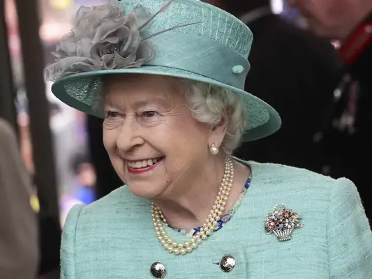 Queen Elizabeth II wears a flower basket brooch, pearls, and hat with floral detail