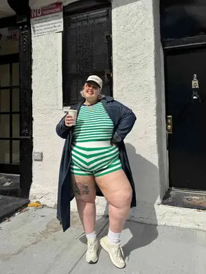 Nataly Osmann wears a white mesh top, a black leather short, sunglasses, a beige trench coat, tights, black leather high heels