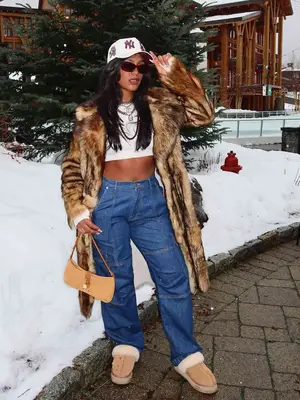 Monet McMichael wearing white NY hat, brown fur coat, high waisted jeans, mini white tee, brown bag, and brown Ugg slippers