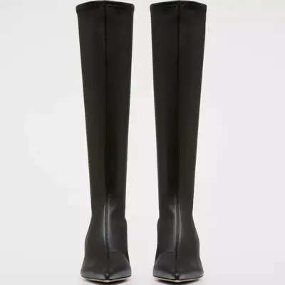 knee-high leather black boots with pointed toe against plain background