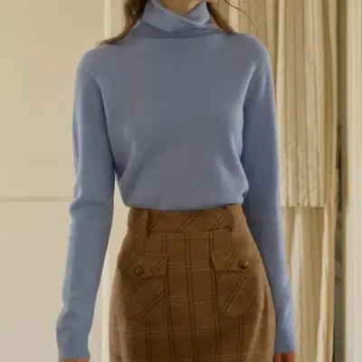 Model wearing a light blue turtlneck and brown plaid skirt 