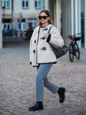 Aline Kaplan wearing a shearling toggle coat, straight leg jeans, boots, and sunglasses - MYM Beauty Fall/Winter 2023 Coat Trends