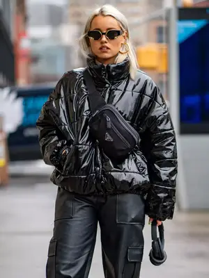 Victoria Moura wearing a glossy black puffer coat, leather cargo pants, and carrying headphones - Fall/Winter Coat Trends MYM Beauty
