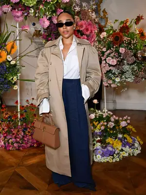 Gigi Vassallo wearing a neutral trench coat, white button down shirt, navy pleated pants, sunglasses, and tan handbag - Fall/Winter Coat Trends MYM Beauty