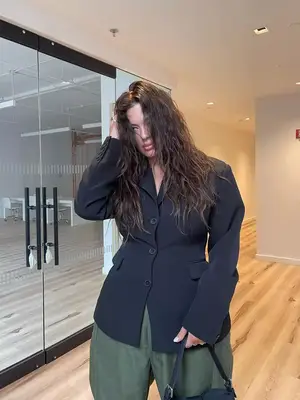 Ashley Graham wears a single-breasted blazer with cinched waist, wide leg pants, and a black handbag