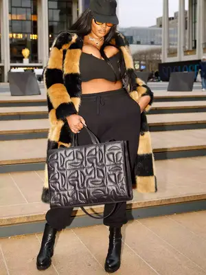Precious Lee wears a brown and tan color block checked coat, black bra and sweatpants, and puffer Telfar bag