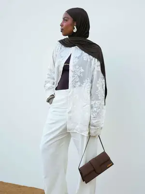 woman wearing white outfit, head scarf, holding brown handbag