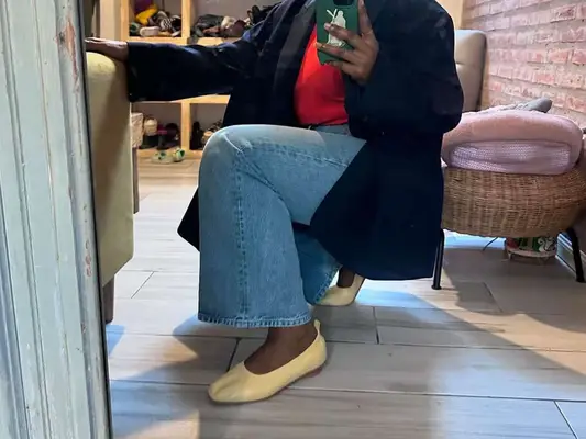 Close-up of woman wearing red top, wide leg jeans, cream flats, and black blazer