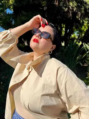 Woman wears button-down shirt, tortoiseshell sunglasses, and red lips and mani