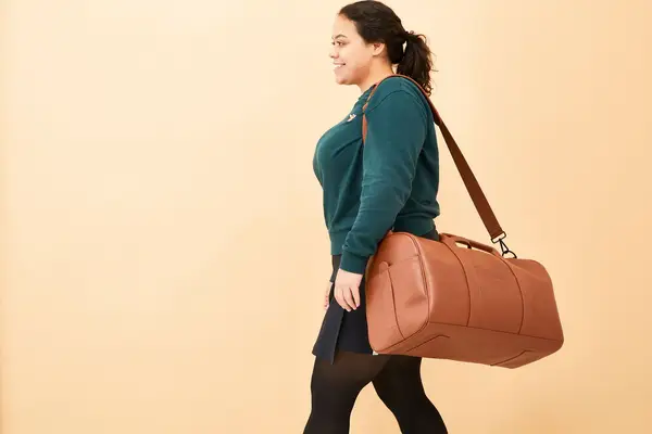 A person carrying the Monos Metro Carry All Duffel by its shoulder strap