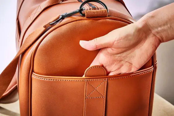 A person placing their hand in the side pocket of the Monos Metro Carry All Duffel