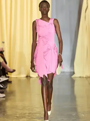 Model walks the Sandy Liang runway wearing a pink dress with subtle bow details, off-white bag and shoes