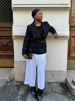Nnenna Echem wears a black blazer and shirt, white linen skirt, black headband, handbag, belt, and boots