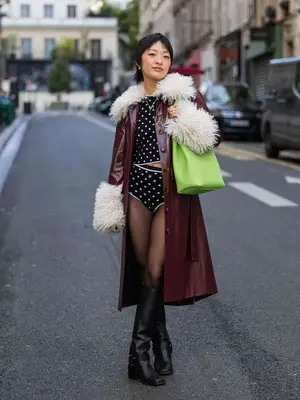 Woman wears a polka dot top, shorts, tights, and burgundy leather jacket with a neon green Lonchamp Le Roseau bucket bag