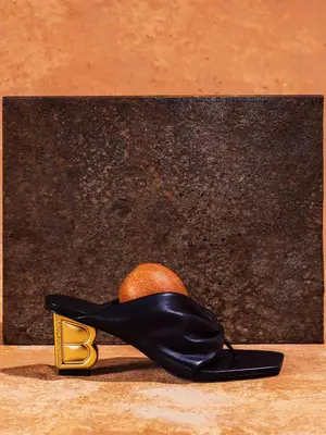 Black thong heeled sandal with gold heel and apple sitting inside