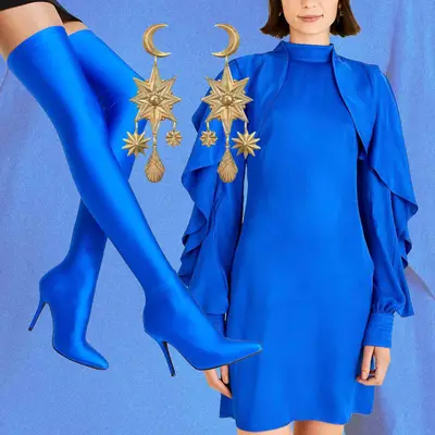 Bright blue dress with ruffled cape sleeve, gold star and moon earrings, and bright blue thigh high boots