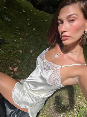 Hailey Bieber wearing a white slip dress, pendant necklace, gold hoop earrings, and leather boots