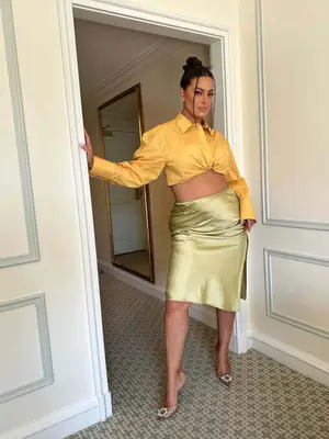 Ashley Graham wears a yellow button-down shirt, green slip skirt, and clear heels with decor