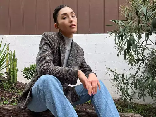 Woman wearing a blazer, turtleneck, jeans, and hoop earrings