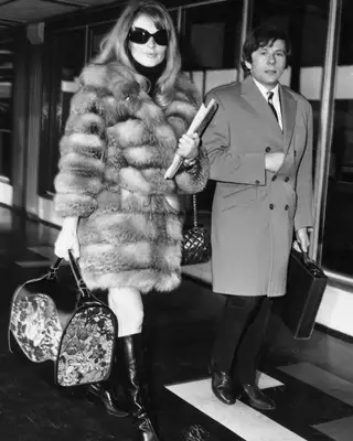 Sharon Tate wearing a fur coat with a floral tote and black boots