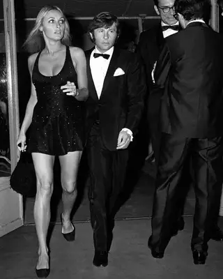 Sharon Tate wearing a sparkly black dress with black flats and handbag