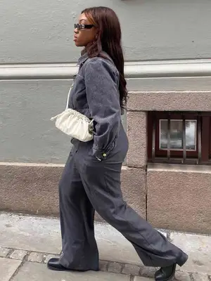 Nnenna Echem wears a gray denim jacket, trousers, black heeled boots, white crossbody bag, and black sunglasses