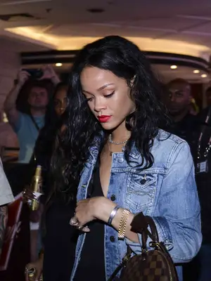 Rihanna wearing a denim jacket, little black dress, Louis Vuitton handbag, and mixed metals jewelry