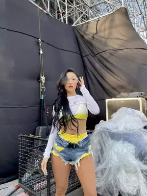 Madison Beer wears a beige linen vest top, black distressed unbuttoned jeans, and sunglasses on head