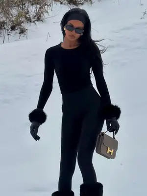 Jasmine Tookes in all black outfit in the snow, holding sage green Hermes handbag