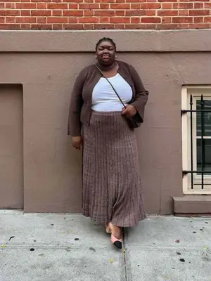 Abisola Omole wearing a brown cardigan, white tank, brown knit skirt, and kitten heels