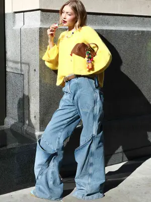 Gigi Hadid wearing a yellow sweater, jeans, and carrying a camel handbag