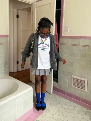 Toni Bravo wearing a gray cardigan, graphic tee, pleated skirt, and blue socks