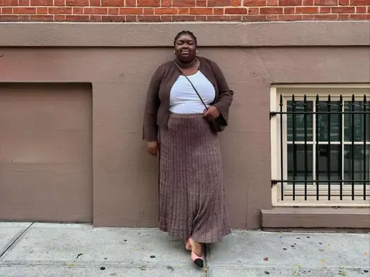 Abisola Omole wearing a white shirt, brown cardigan, and brown rib knit skirt
