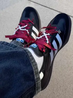 Person wearing black Adidas Sambas sneakers with dark red ribbon as shoelaces and pearl string accents