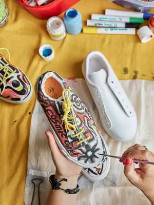 Person painting a white pair of sneakers with black and red paint