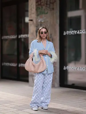 Sonia Lyson is seen wearing several silver and golden earrings; oval sunglasses with golden frame from Celine; a golden necklace with two interwoven rings; a light blue pajama shirt with yellow piping along the seams and yellow ostrich feather cuffs; the beige braided leather bag âJodieâ from Bottega Veneta; wide jeans in denim checkerboard pattern from Bershka; two yellow-gold âLoveâ bracelets from Cartier; another golden bracelet and light blue denim loafers