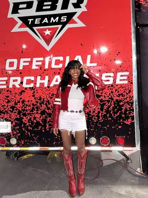 Woman wearing white top, white denim shorts, red cowboy boots, and red and white moto jacket
