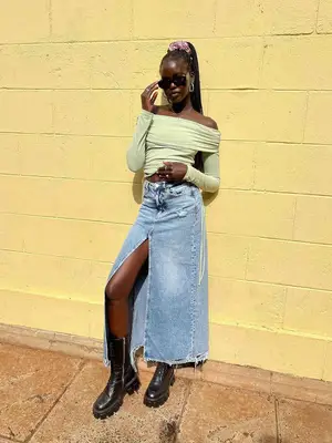 Adut Akech Bior wearing a light green off-the-shoulder top, denim maxi skirt, and black boots. 