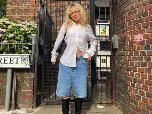 Sabrina Carpenter wearing a white button-down shirt, denim bermuda shorts, black boots, and black shoulder bag