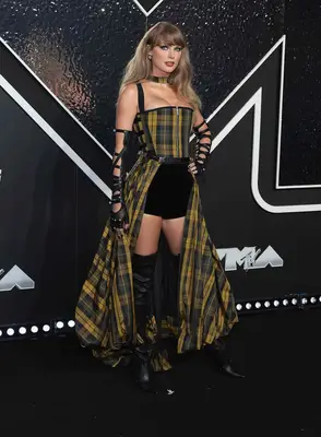 Taylor Swift wears a yellow and black plaid Dior gown , strapped fingerless opera gloves, and black knee-high boots to the 2024 VMAs