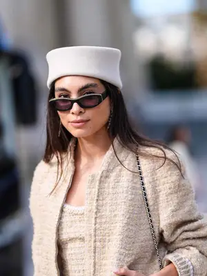 Woman wearing white pillbox hat, black sunglasses, tweed top and jacket, and Chanel handbag