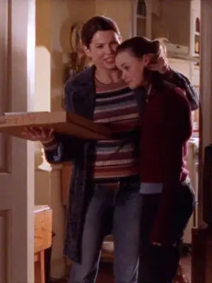 Lorelai Gilmore hugs Rory while wearing a multicolored striped sweater and carrying a pizza box
